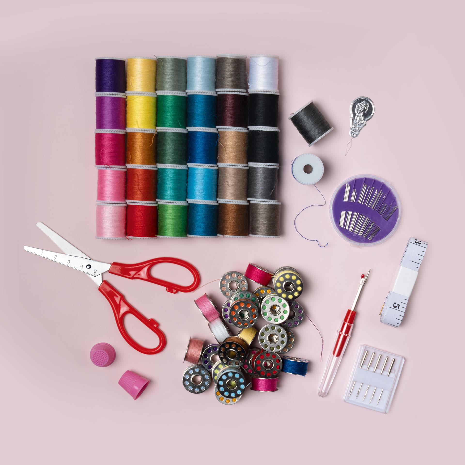 Transparente Box mit bunten Garnspulen, Metallspulen, Nadeln und Nähzubehör