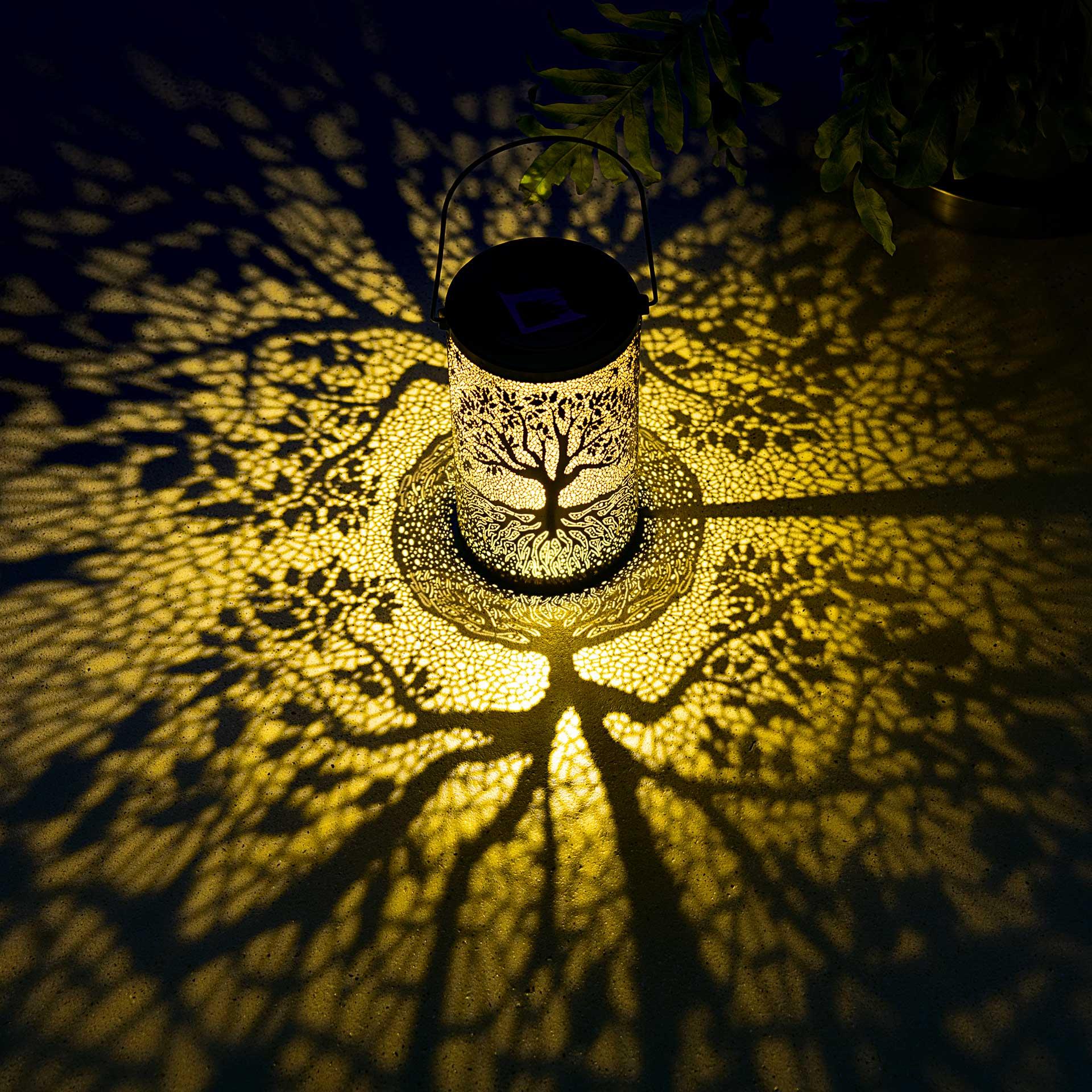 Eine zylindrische Solarlaterne mit einem kunstvoll ausgestanzten Baum-des-Lebens-Motiv und einem Metallhenkel zum Aufhängen