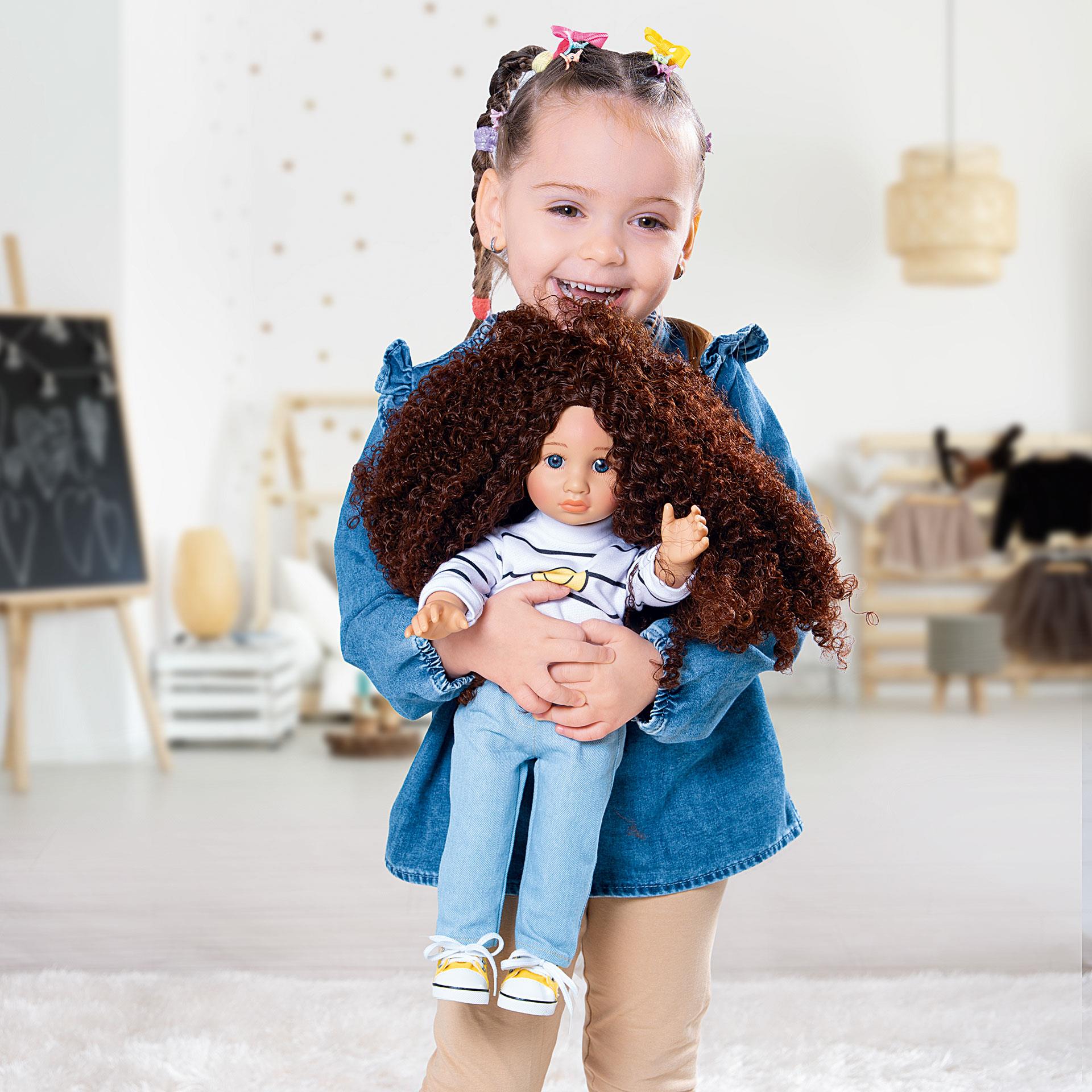 Spielpuppe mit braunen lockigen Haaren, gestreiftem Pullover mit Smiley, hellblauen Jeans und gelben Sneakers